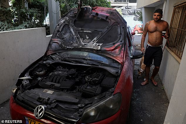 A Tel Aviv man stands next to a damaged car near the site of a deadly explosion, amid the conflict between Israel and Hamas in Tel Aviv.