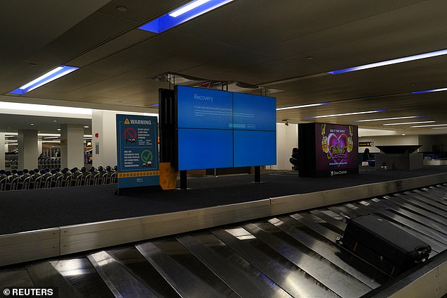 A piece of checked luggage is seen near a monitor displaying a blue error screen at a baggage claim area inside Newark International Airport.