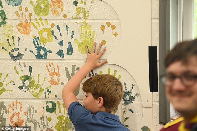 George spreads blue paint on his hand and presses it against a wall to leave a handprint at Big Help Out in Slough.