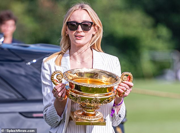 A crowd of onlookers smiled as the star held the large golden cup in front of a luxury vehicle.