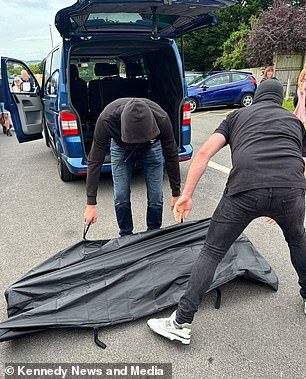 Men wearing balaclavas prepare to unzip one of the bags.