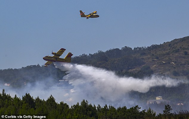 Two Canadair CL-215 (Scooper) amphibious firefighting aircraft fly over a dense cloud of smoke to drop water on a large forest fire in Portugal