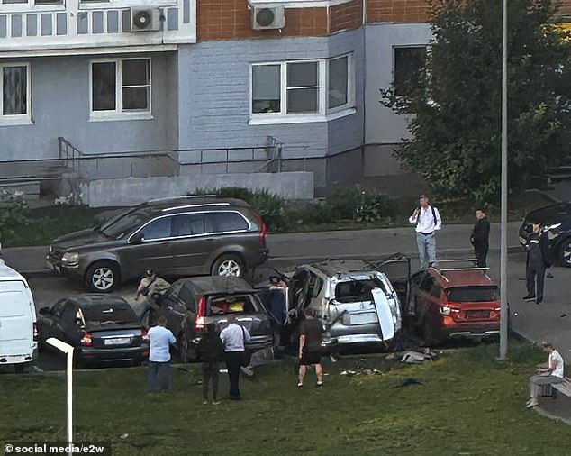 Community members gather around the car that exploded on Sinyavinskaya Street in northern Moscow.