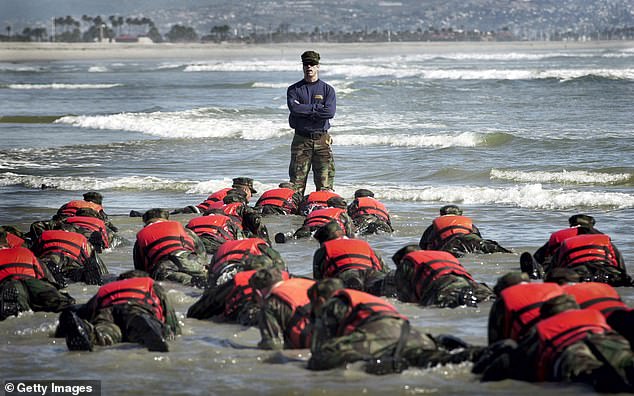 A Navy SEAL instructor assists Basic Underwater Demolition/SEA students