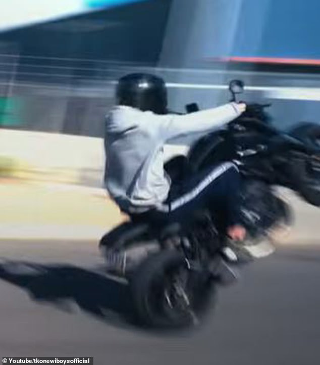 The music clip shows motorbikes doing wheelies (pictured) and cars burning tyres on a road in an industrial area.