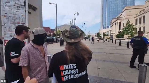 The men are dressed in T-shirts that say 'Whites Against Replacement', while one man wears a face mask with a swastika emblazoned on it.