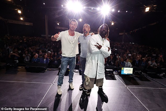 Hemsworth took the stage in Hall H of the San Diego Convention Center wearing a white T-shirt under a white, short-sleeved button-down shirt with a long gold chain.