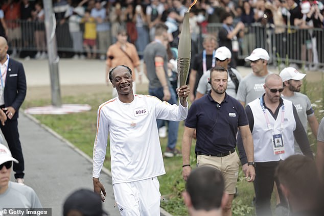 The rapper, who will be part of NBC's coverage of the Games, was all smiles as he walked with the torch in hand.