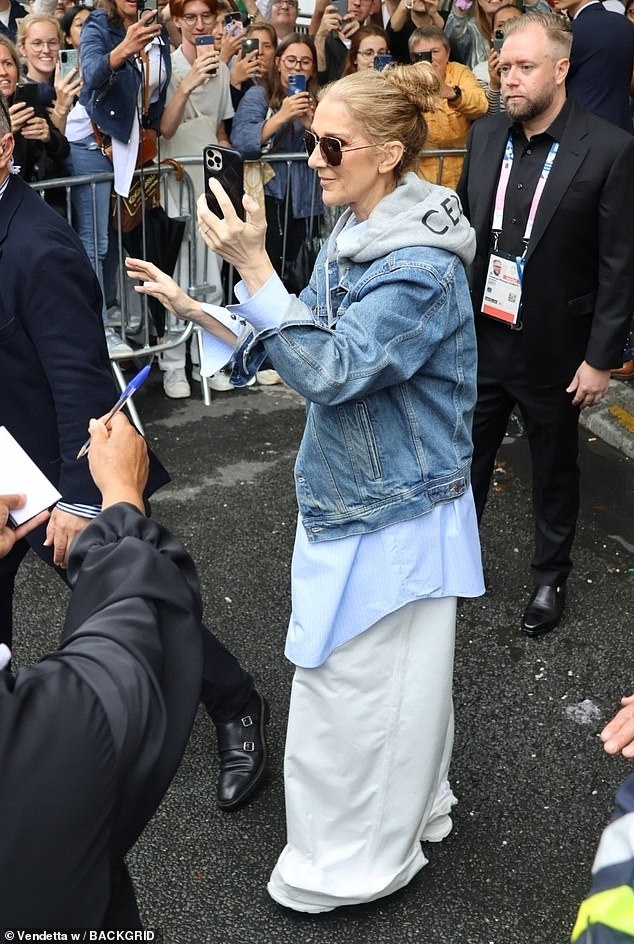 Cutting a casual figure in flared white linen trousers, a blue shirt and a grey hoodie which she layered under a denim jacket.