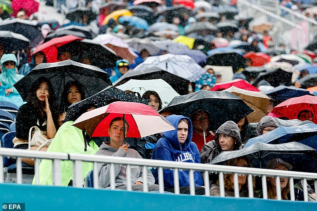 Spectators use umbrellas and raincoats to protect themselves from the rain during the opening ceremony.