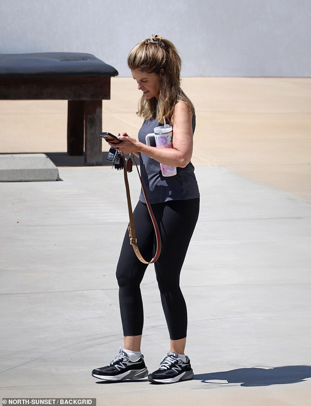 The former first lady of California, 68, was similarly dressed in a grey tank top and black leggings with the beach pictured behind her as she looked at her phone while carrying a Stanley cup under her arm.