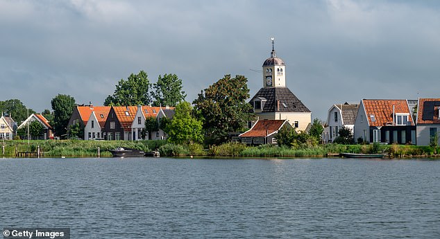 Pictured: Church and houses on the dyke of the village of Durgerdam from the river Buiten IJ near Amsterdam, Netherlands