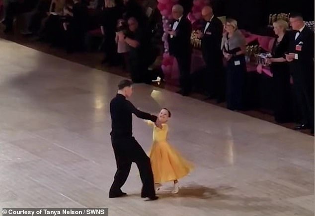 Amelia appears in the photo wearing a yellow dress with her dance partner in a competition.