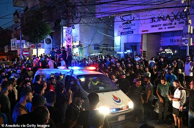 An ambulance makes its way through the crowd. Video footage showed a burning apartment building and a sense of panic in the southern suburb of Haret Hreik this evening.