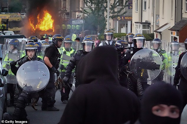 Riot police with shields and helmets hold back protesters after disorder breaks out