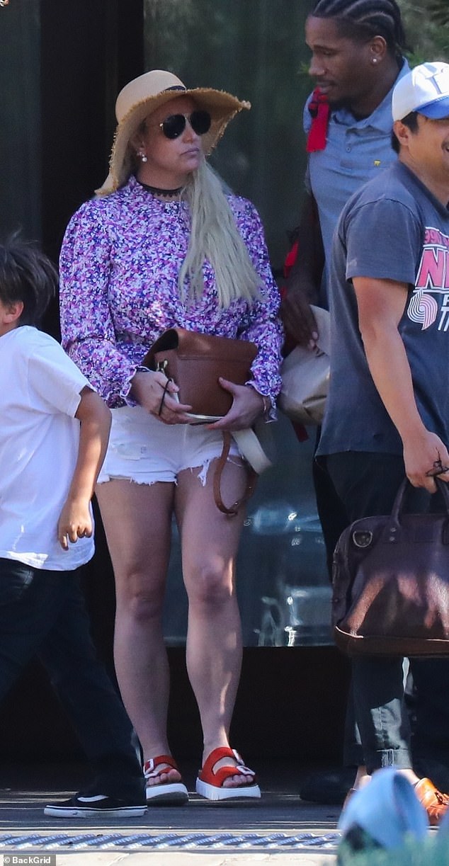 Britney cut a casual figure in a purple and white top and white denim shorts, along with a straw hat and slip-on sandals.