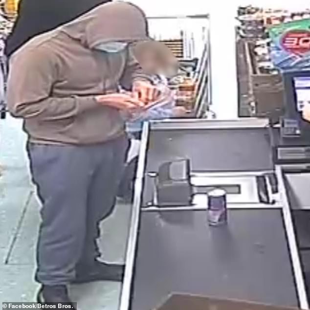 The man, wearing a hoodie and face mask (pictured), was caught on CCTV footage walking towards the till with a bottle of water and a can of Red Bull.