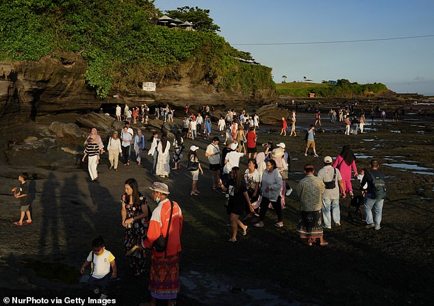 Bali's tourism minister wants tourists to be more spread out across the island, but he doesn't want locals to protest against visitors (pictured, tourists in Bali visiting the Pura Batu temple in Bali)