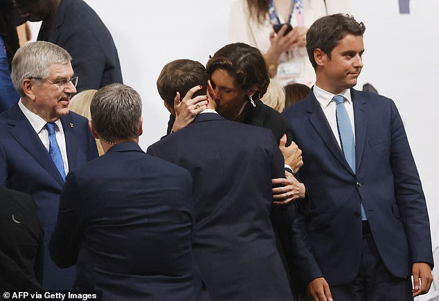 French Prime Minister Gabriel Attal can be seen on the right, looking away as the two exchange a close kiss.