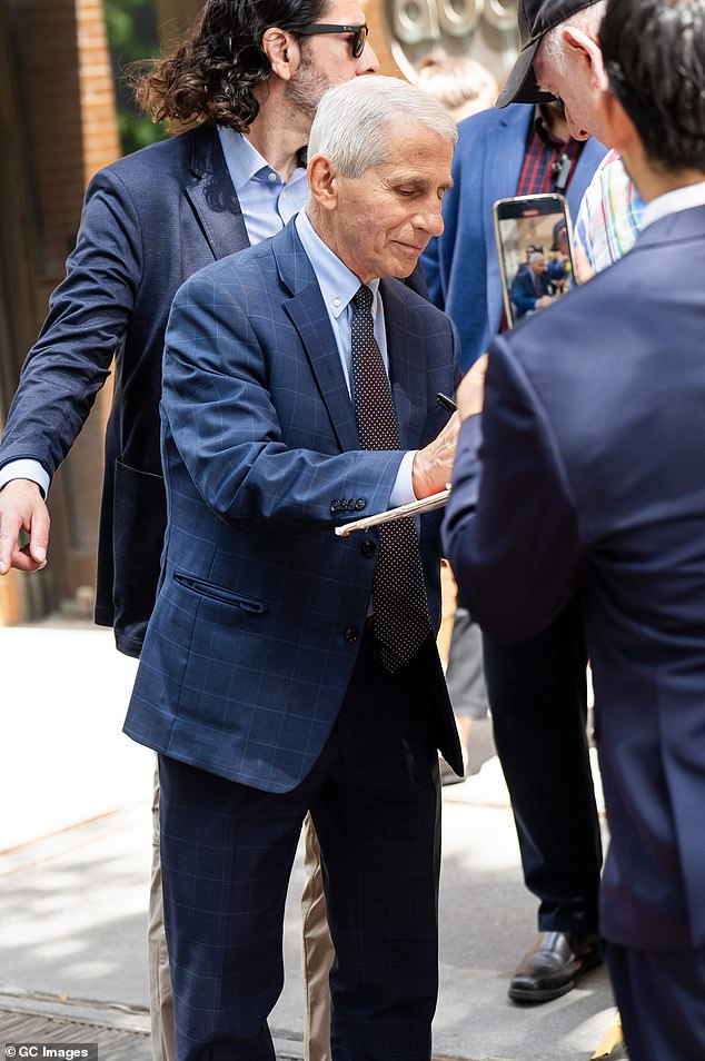 Fauci signs autographs outside ABC studios in New York with a member of his team of U.S. Marshals behind him.