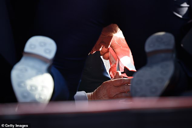 An extraordinary photograph shows Donald Trump on the ground at the Butler Show Grounds in Pennsylvania on Saturday after he was injured in a shooting that left two people dead.