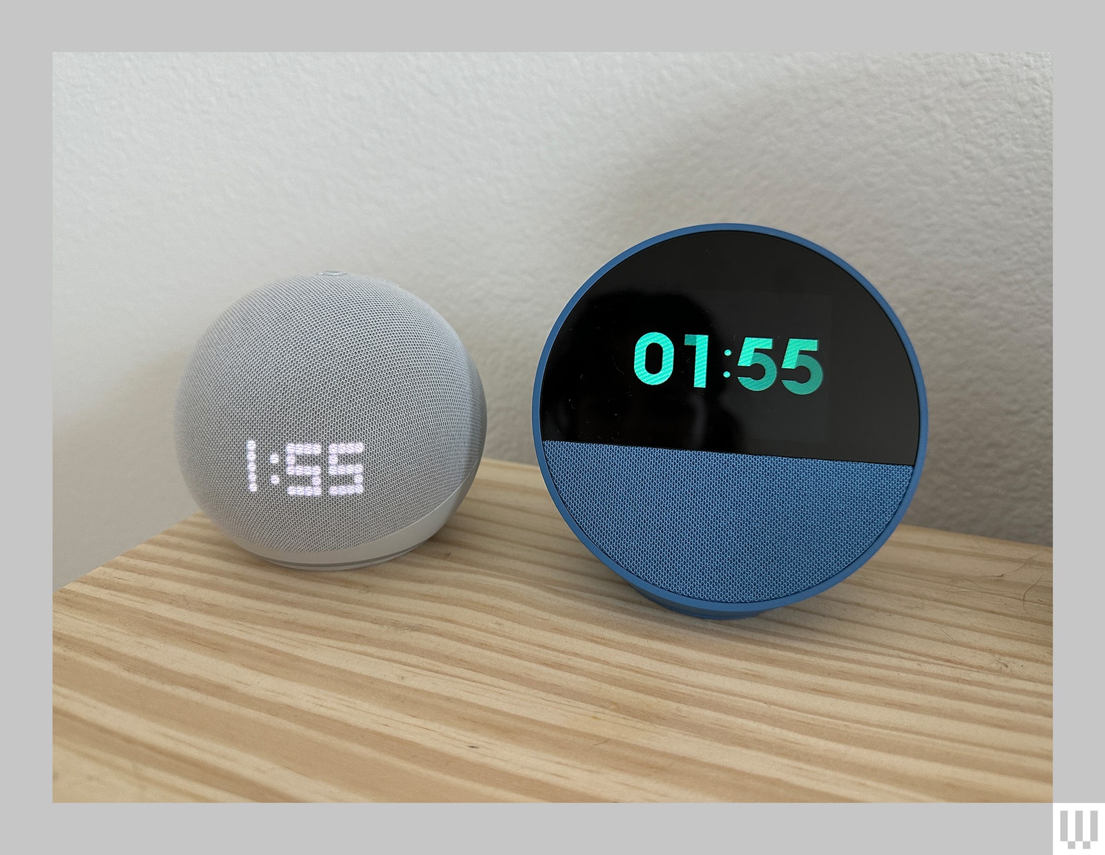 A white sphere-shaped device that displays the time next to a blue semi-sphere-shaped device that also displays the time. Both sitting...