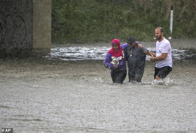 A man helps two people walk through floodwaters after their car became stuck on Vandeventer Avenue under I-64 (Hwy. 40) in St. Louis, Mo., Thursday, July 28, 2022.