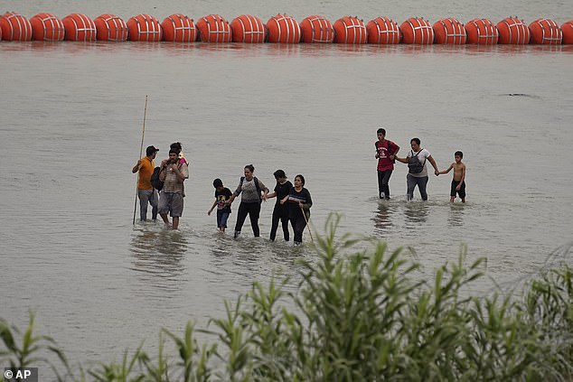 Migrants crossing the Rio Grande from Mexico pass by large buoys being deployed as a border barrier