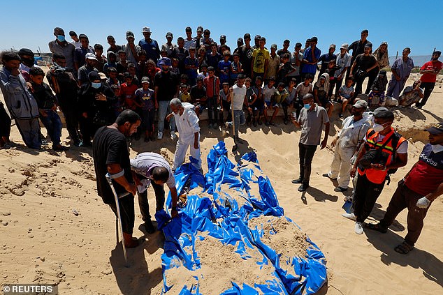 People watch as bodies of unidentified Palestinians are buried in a mass grave after Israel handed them over, amid the conflict between Israel and Hamas, in Khan Younis, southern Gaza Strip, August 5, 2024.