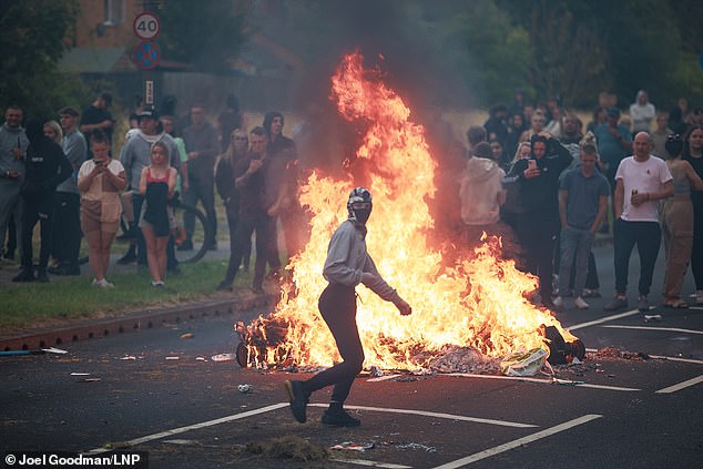 A masked rioter runs past a bonfire in the middle of the street in Rotherham on Sunday