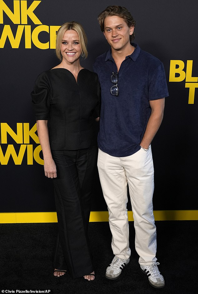 Deacon looked handsome in a navy velvet collared shirt, white pants, matching sneakers, and a pair of glasses hanging around his neck.