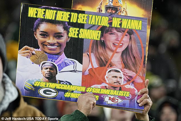 A Green Bay Packers fan holds a sign featuring Taylor Swift and Simone Biles in 2023