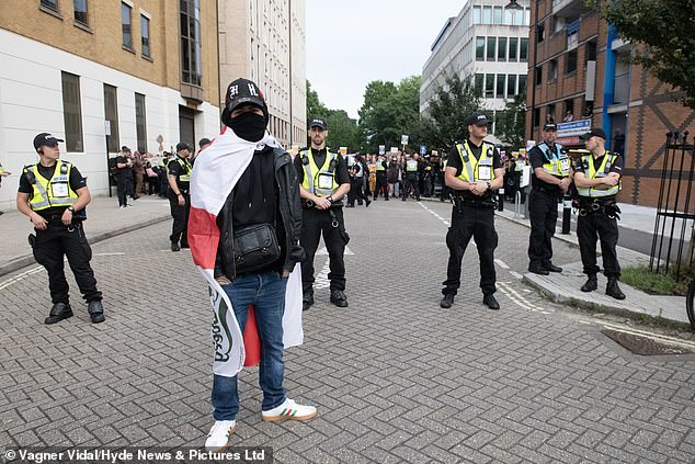 A man wrapped in an England flag stands facing police officers in Southampton, as a large group of anti-racism protesters gather behind him.