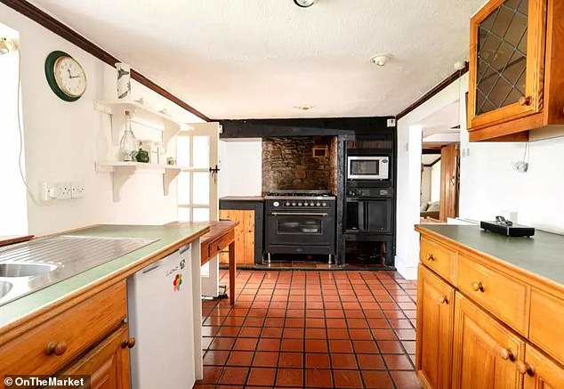 The kitchen is currently fitted with a gas hob and built-in oven and microwave, set amongst 1970s-style cabinets.