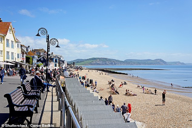 Serene: Holidaymakers relax on the beach and promenade at Lyme Regis