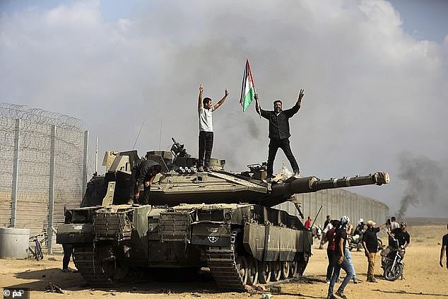 Palestinians wave their national flag and celebrate next to a destroyed Israeli tank at the Gaza Strip fence east of Khan Younis, south, Saturday, October 7, 2023