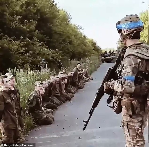 A Ukrainian soldier stands guard as he watches a line of captured Russian prisoners of war in Kursk.