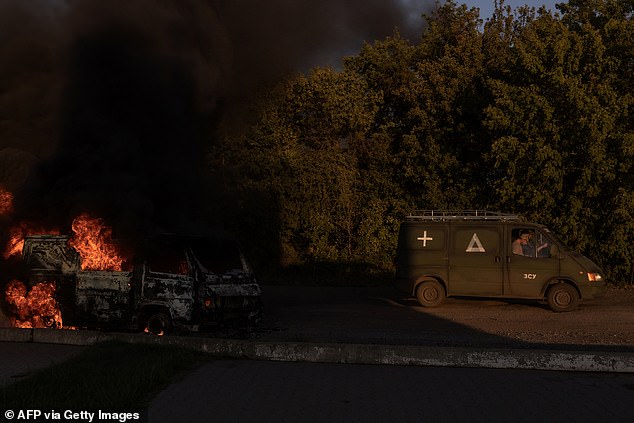 A Ukrainian military vehicle drives past a burning car on a highway near the border with Russia, in Sumy region, Ukraine, August 14, 2024.