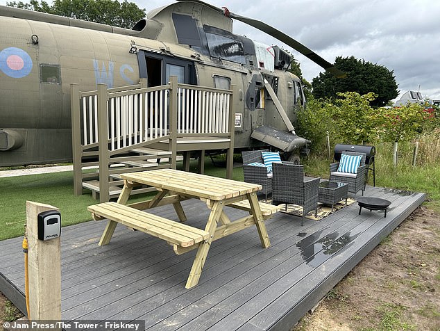 Outside the helicopter is a covered area with a picnic bench, rattan table and chairs, as well as a barbecue and fire pit (above).