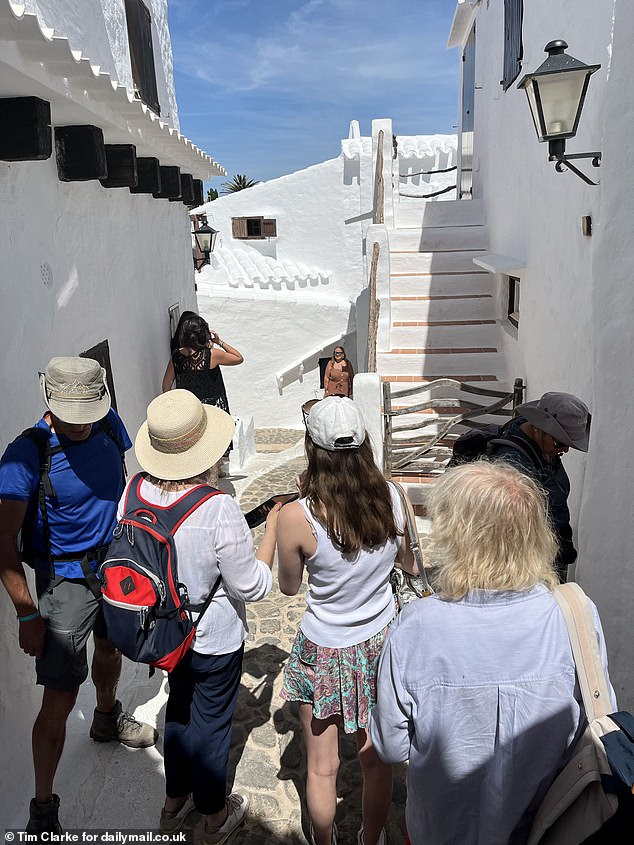 A crowd of tourists is seen crowding into a small alley in the village to take photos in front of the picturesque white stone houses.