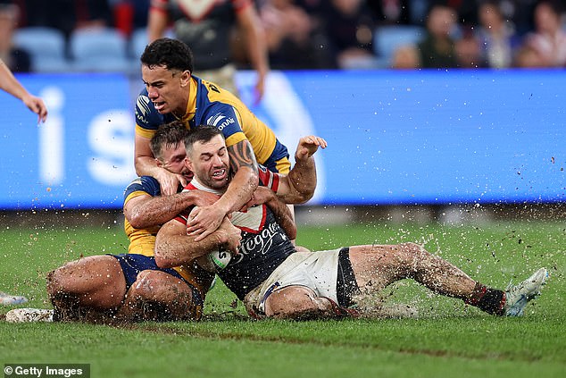 Roosters captain James Tedesco is tackled as mud and water fly from the surface.