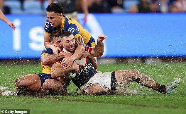 Roosters captain James Tedesco is tackled as mud and water fly from the surface.