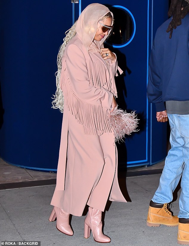 She continued to embrace her inner cowgirl in a pastel pink tasseled fringe coat and added a semi-sheer scarf that she wrapped around her head.