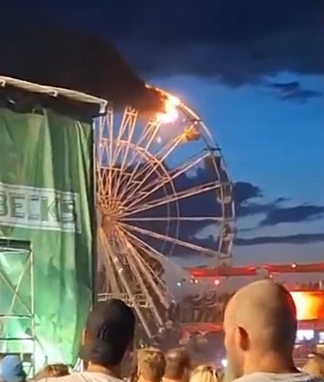 Black smoke billows from one of the upper carriages as festival-goers look on.