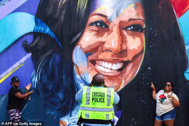 A Chicago police officer takes a picture of people posing next to a mural of Harris outside the United Center that was put up in preparation for the Democratic National Convention (DNC) this week.