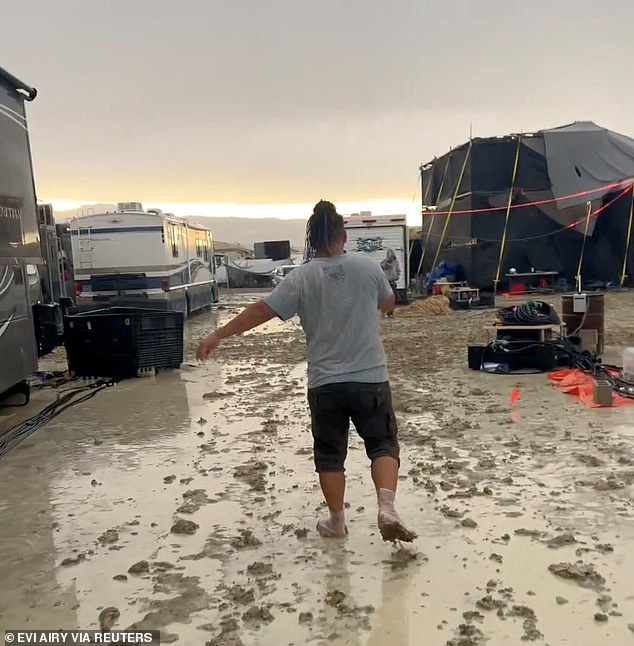 Attendees were initially ordered not to leave after exit routes were rendered impassable by half an inch of rain. (pictured: a reveller wading through thick mud at the festival last year)