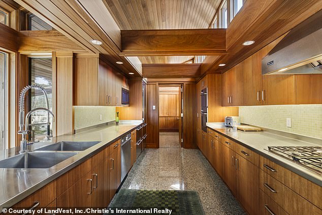 The gourmet galley-style kitchen (pictured) has a large gas stove, stainless steel range hood, thick wood beams above, granite floors, and more modern stainless steel appliances.