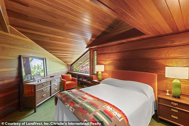 Another smaller bedroom, also covered in wood, is equipped with abstractly shaped sloped ceilings, windows, and space for a queen-size bed.