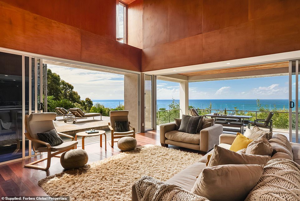 The living room features double-height ceilings in soft honey tones with an open fireplace.