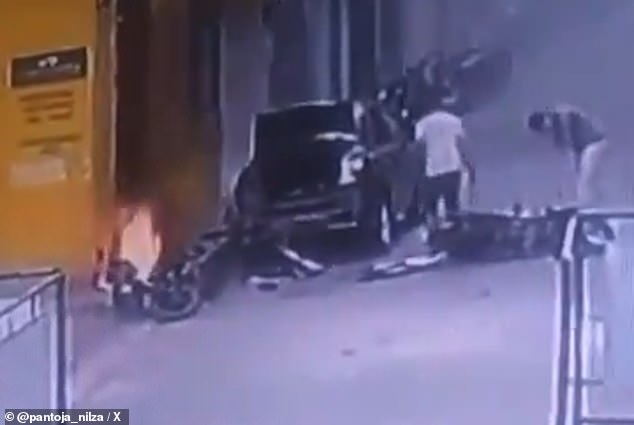 Two teenagers stand near their wrecked motorbike which was left lying on the ground after a motorbike bomb attack (pictured, on fire, left). The teenagers were taken to a local medical centre where they received treatment. The severity of their injuries is not known.